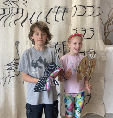 Two children stand smiling with hand-held puppets, one owl and one lapwing.
