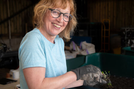 Volunteer smiling whilst potting on plants in the nursery